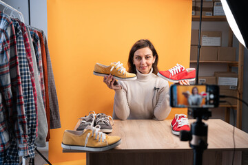 Young woman blogger looking at camera showing sports shoes, works in internet store. Modern...
