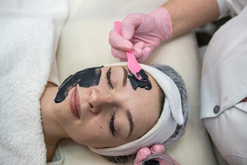 female lying at bad on spa clinic and receive cream black cosmetic mask