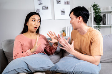 Upset Asian boyfriend and girlfriend sitting together on sofa at home after having quarrel and fight at home. Offended married couple in silence after relationship problem