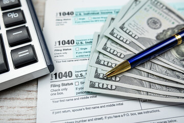 business accounting concept - 1040 tax form with pen calculator us dollar bills