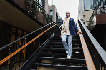 Young african woman with short hair wears trendy outfit going down the stairs