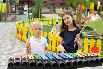 Children play with a hammer on a street musical instrument, a multicolored xylophone in the park.