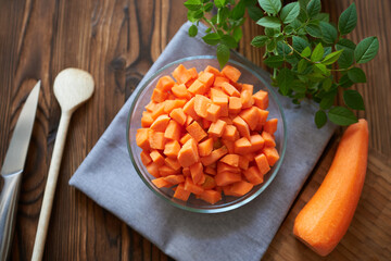 Dicing carrots in a glass bowl, top view. Concept - preparation for cooking, carrots with knife and wooden spoon.