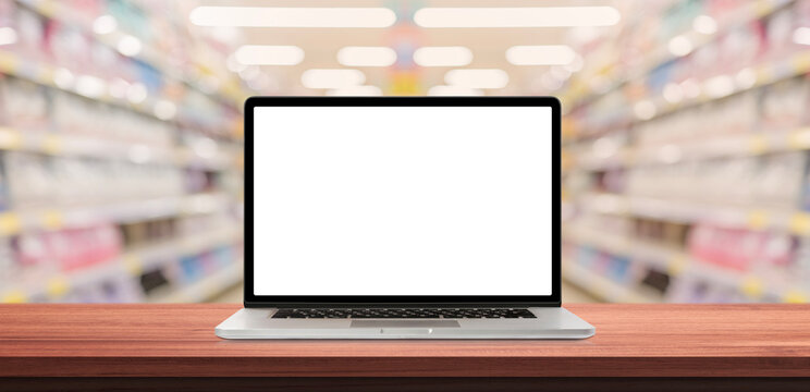 Laptop or notebook with blank screen on wood table in blurry background with shelves in supermarket