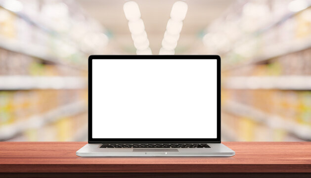 Laptop or notebook with blank screen on wood table in blurry background with shelves in supermarket