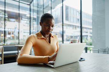 Young african woman freelancer working on laptop while sitting in coworking