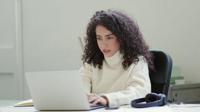 Focused young latin professional business woman office worker using laptop computer working online, browsing tech web services, checking internet marketing project or elearning sitting at desk.