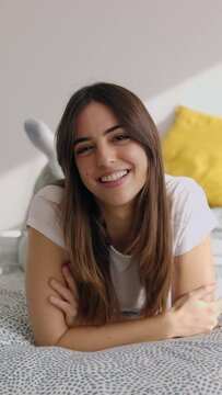 Vertical video portrait of happy pretty young woman smiling at camera while relaxing on bed. Beautiful and cheerful people concept
