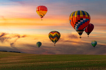 Colorful hot air balloons flying over field at sunset.