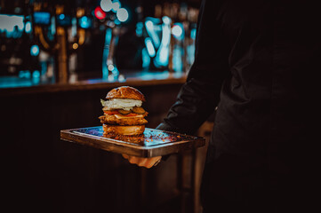 Men's waiter hands hold a tray with a cheeseburger in pub