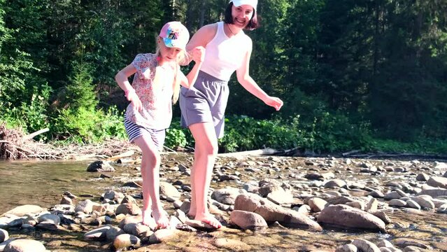 mother with daughter walking barefoot by rocks at mountain river