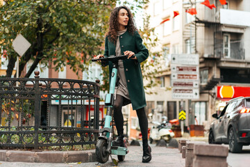 Naklejka premium Young curly woman with electric scooter at the city