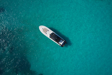 White modern boat with motor on blue transparent water aerial view. Big white motor boat anchored...