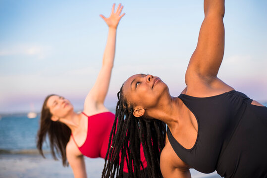 Women doing yoga in Triangle Pose (Trikonasana) on beach, Newport, Rhode Island, USA