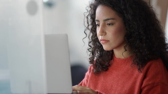 Young busy latin business woman office worker, company employee or student using laptop, typing on computer sitting in office elearning course looking at pc, thinking on data operations plan.