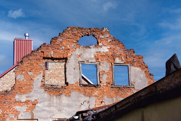 Old abandoned red brick residential building wall with windows holes without roof with visible blue sky and white clouds background