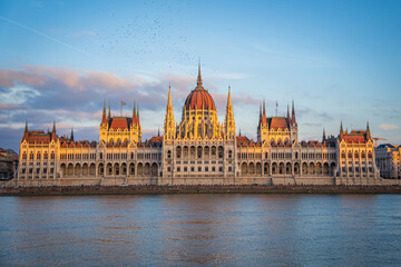 Fototapeta na wymiar Budapest Parliament from across Danube river at Sunset, Hungary. Beautiful golden light on building rooftop. Evening sky with pink clouds.