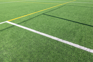White and yellow stripes on green soccer field from side view. Artificial turf on football field. Green synthetic grass on sport ground with shadow from soccer goal net
