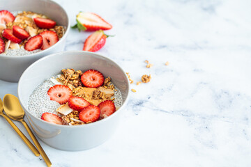 Chia pudding with homemade coconut granola, peanut butter and strawberries in a gray bowl, marble background. Healthy diet, detox, summer recipe.