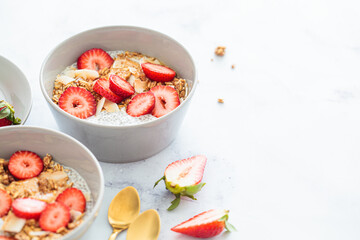 Chia pudding with homemade coconut granola, peanut butter and strawberries in a gray bowl, marble background. Healthy diet, detox, summer recipe.
