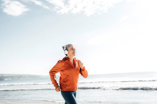 Smiling woman wearing headphones jogging at beach