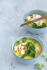 Vegan laksa with rice noodles, broccoli and tofu in blue bowls, gray background.
