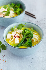 Vegan laksa with rice noodles, broccoli and tofu in blue bowls, gray background.