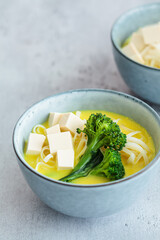 Vegan laksa with rice noodles, broccoli and tofu in blue bowls, gray background.