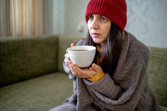 Woman wrapped in blanket sitting with cup of tea at home
