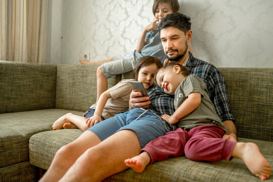 Father sharing smart phone with sons sitting on sofa at home