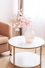 Soft home decor in soft tones, a pink vase with pink beautiful flowers on the background of a window and pink curtains, round table. Interior.	