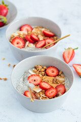 Chia pudding with homemade coconut granola, peanut butter and strawberries in a gray bowl, marble background. Healthy diet, detox, summer recipe.