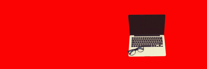 Laptop with blank black screen and eyeglasses on red background, copy space for advertising text