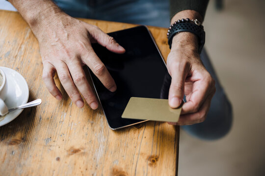 Man holding credit card using tablet PC on table in cafe