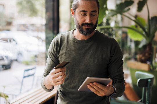 Bearded man holding credit card using tablet PC in cafe