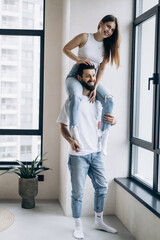 Fototapeta na wymiar A young cute couple in white t-shirts and blue jeans stand in a new apartment and rejoice in happiness.