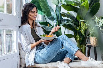 Happy woman eating salad at the window