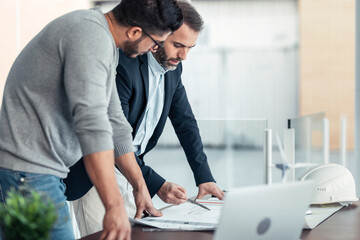 Architects having discussion over blueprint on desk at office