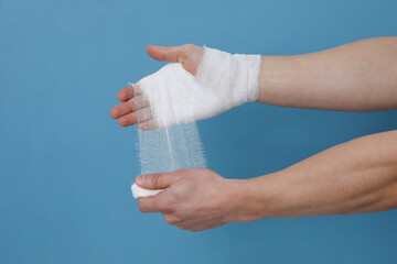 Concept of help during an injury, man wrapping hand in bandage on blue background