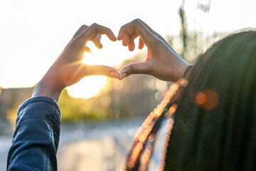 Woman gesturing heart shape at sunset