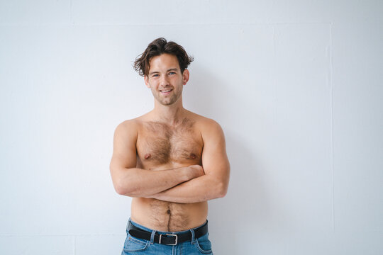 Smiling shirtless man standing in front of white wall