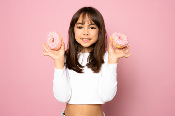 Pretty little girl having fun with some sweet food holding a couple of donuts and smiling isolated over pink background.