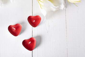 Candles in the form of red hearts on a light wooden background