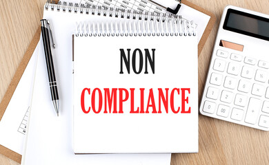 NON COMLIANCE is written in white notepad near a calculator, clipboard and pen. Business concept