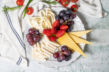 Cold cheese plate, cheese set platter. Strawberry, grape and cheese assortment on gray background. Top view