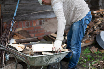 A man puts firewood from a cart into a firewood storage