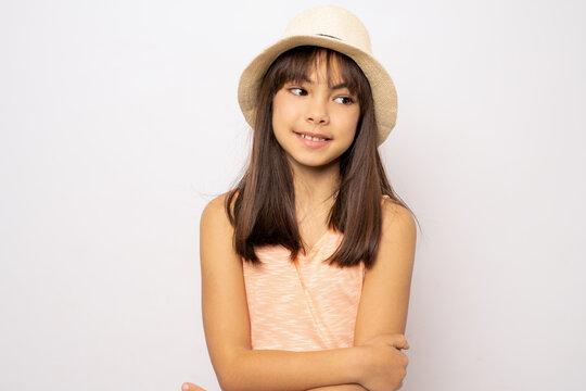Smiling little brunette girl wearing straw hat posing with arms folded isolated over white background.