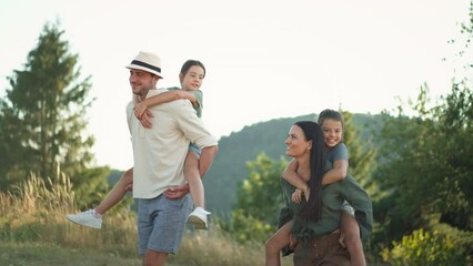 Happy parents giving their children piggyback ride in summer in nature.