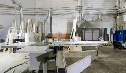 A large sliding table saw machine with dust hood in industrial factory producing wooden furniture...