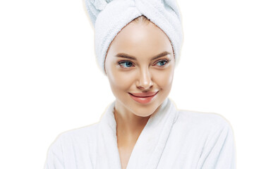 Day spa, beauty and freshness concept. Pensive European woman with healthy skin concentrated aside thoughtfully, feels refreshed after bath procedures, dressed in dressing gown, towel on head